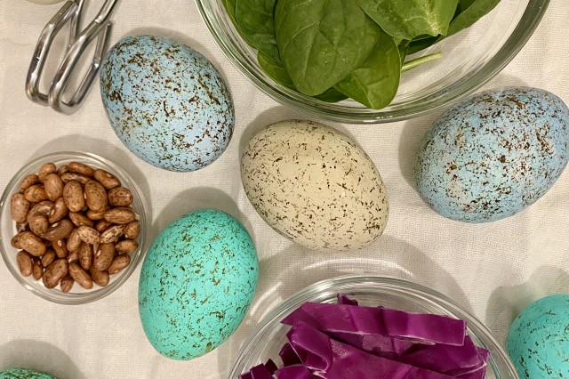 4 speckled eggs on a table surrounded by spinach, nuts, and cabbage