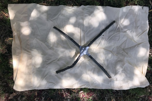 Coloca los dos palitos formando una &quot;X&quot; sobre la tela y sujétalos juntos en el medio.