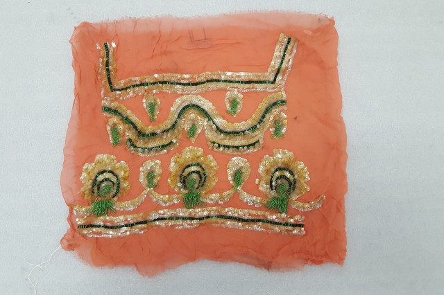 Embroidery sample on orange tulle with gold and green pattern