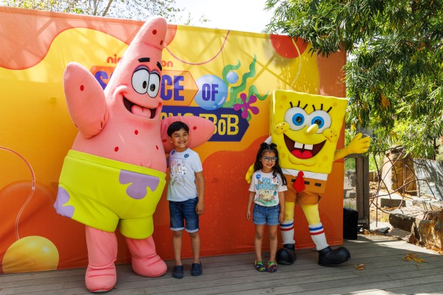 Pink cone-shaped and yellow square costumed figures standing with two children