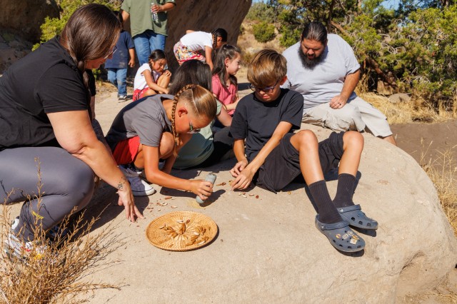 Family groups are on top of a bedrock mortar grinding acorns