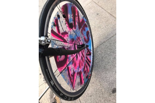 Bicycle wheel spokes decorated with a circular sign spraypainted with the pink and black words: &quot;Black Lives&quot;