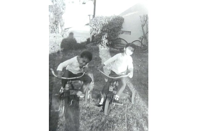 Black and white photo of two young girls of color on tricycles in their backyard