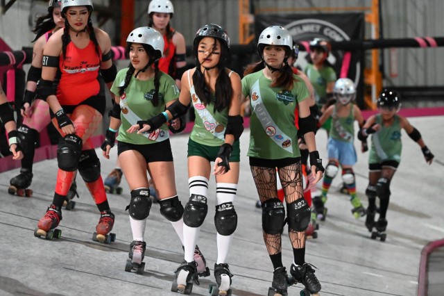 Teenage girls in green vs. red uniforms skating around a banked roller derby track