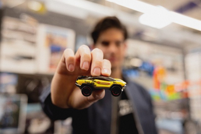 A man holds up a yellow and black Hot Wheel racecar with the number 9 and the text 'Angulo Racing'