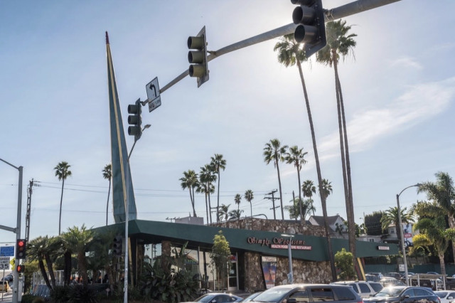 The iconic Googie-style architecture of Simply Wholesome, featuring its signature sloped roof and mid-century modern design surrounded by palm trees.