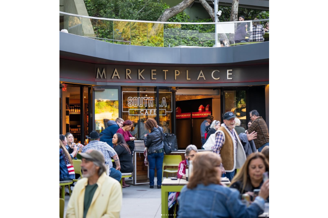 Crowd sitting outside a coffee shop with the sign "Marketplace" above the entrance.