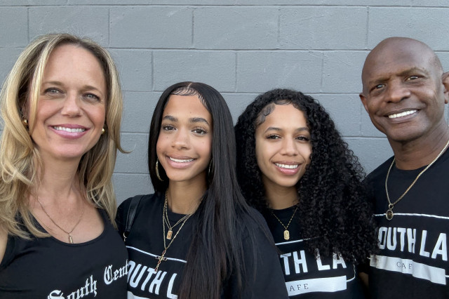 Mixed race family, mother and father standing on either side of their two young daughters, all wearing South LA Cafe-branded shirts.