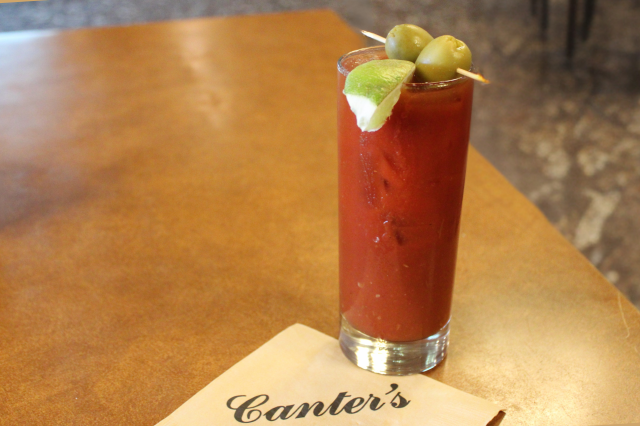 Garnished bloody mary cocktail sitting on top of a Canter's-branded napkin with the retro style restaurant in the background.