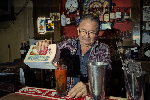 Bartender making a bloody mary cocktail behind the bar.