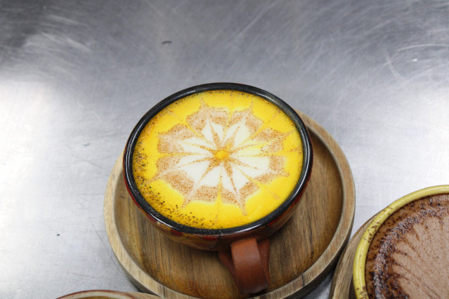 A golden latte from Ulew sits on a stainless steel countertop in a beautiful decorated ceramic mug 