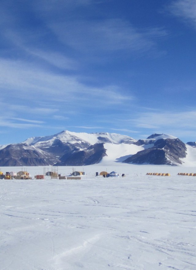 Landscape of snow, mountains, and researchers&#039; tents and field camp under a blue sky 