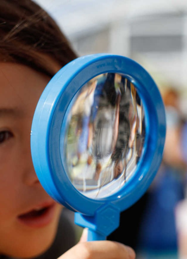 Child looking at a spider through a magnifying glass in the Spider Pavilion