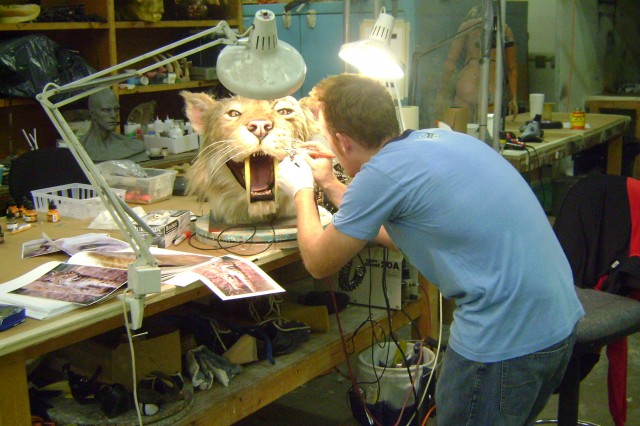 Craftsman making repairs to head of smilodon puppet
