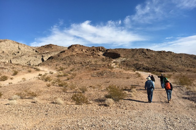 Scientists hiking a mountainous trail to a cave in the distance.