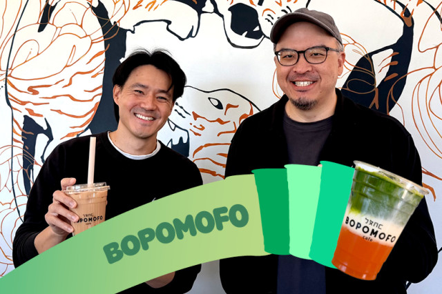 Two mem standing with a colorful drink in hand and in the forefront, again wall with graphic design 