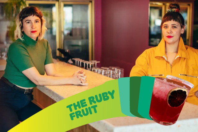 Two people pose behind a long counter inside The Ruby Fruit. One wears a green top and dark pants, while the other wears a bright yellow jumpsuit. In the foreground, a lime green graphic banner features the bar's name next to an image of a red cocktail garnished with a dehydrated citrus wheel.