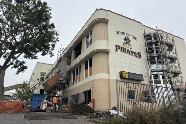 A high school building with the words 'San Pedro Pirates' surrounding an image of a pirate mascot on the building. Signs of construction surround the building 