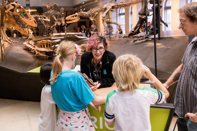 Museum Educator showing a specimen to visitors gathered around a cart