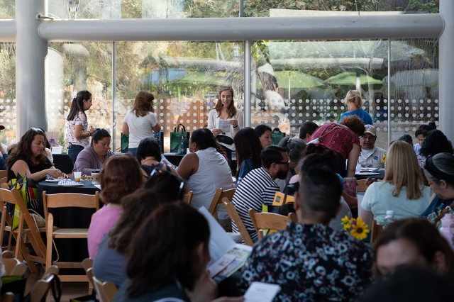 Educators sitting at round tables facing a speaker wearing a headset