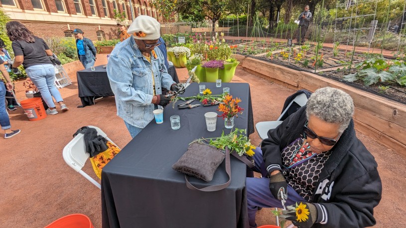 Two women sitting at a table outdoors making flower arrangements in mason jars