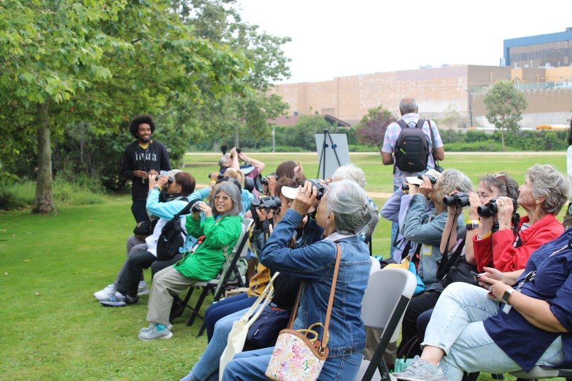 Seniors sitting in chairs in a park, using binoculars to look for birds