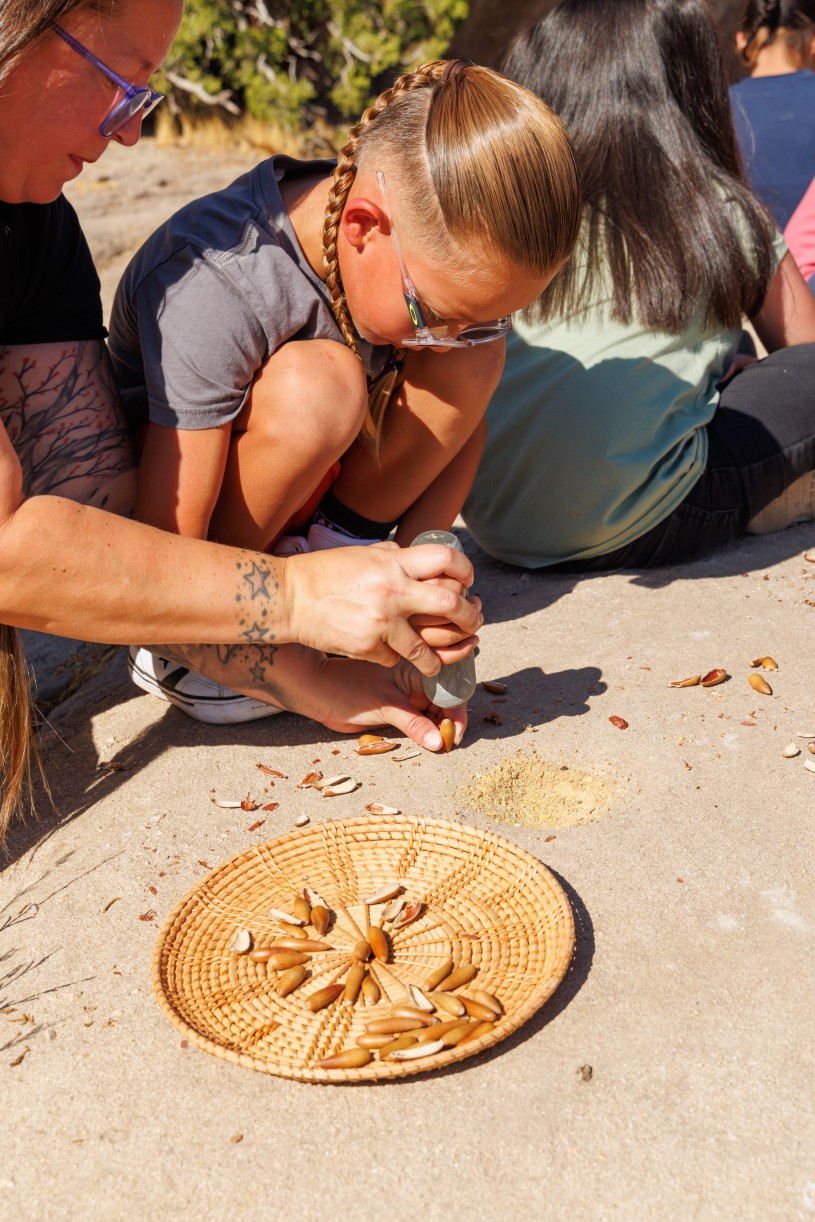 Tiffanie Rayas guides her son'd hand as she shows him how to crack an acorn using a stone pestle and a bedrock mortar. 