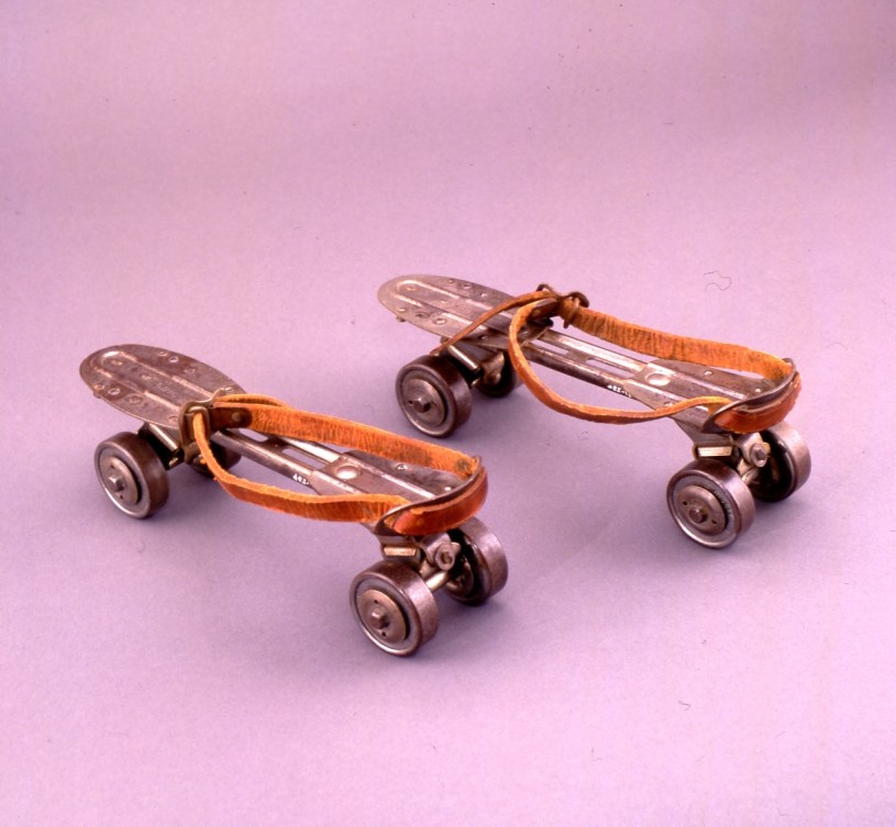 Antique roller skates made of a leather strap attached to a metal plate with four wheels to wear with regular shoes.