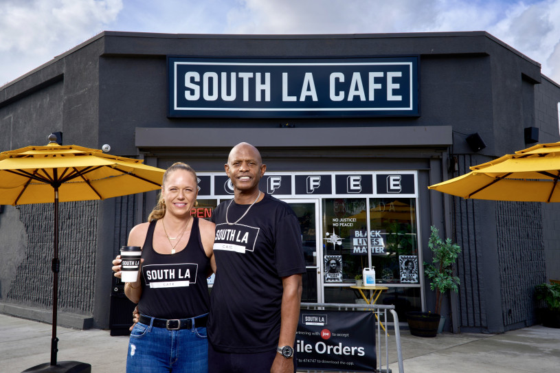 South LA Cafe co-founders Joe and Celia Ward-Wallace posing outside their original location at Browning and Western, wearing black branded shirts.